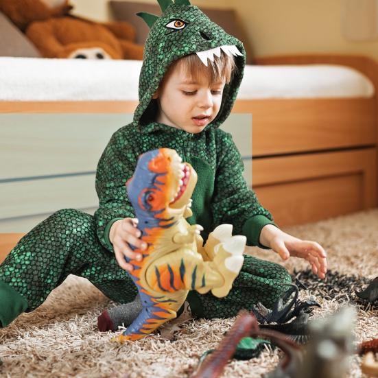 Barn i grøn dinosaurdragt leger med dinosaurfigurer på gulvet.